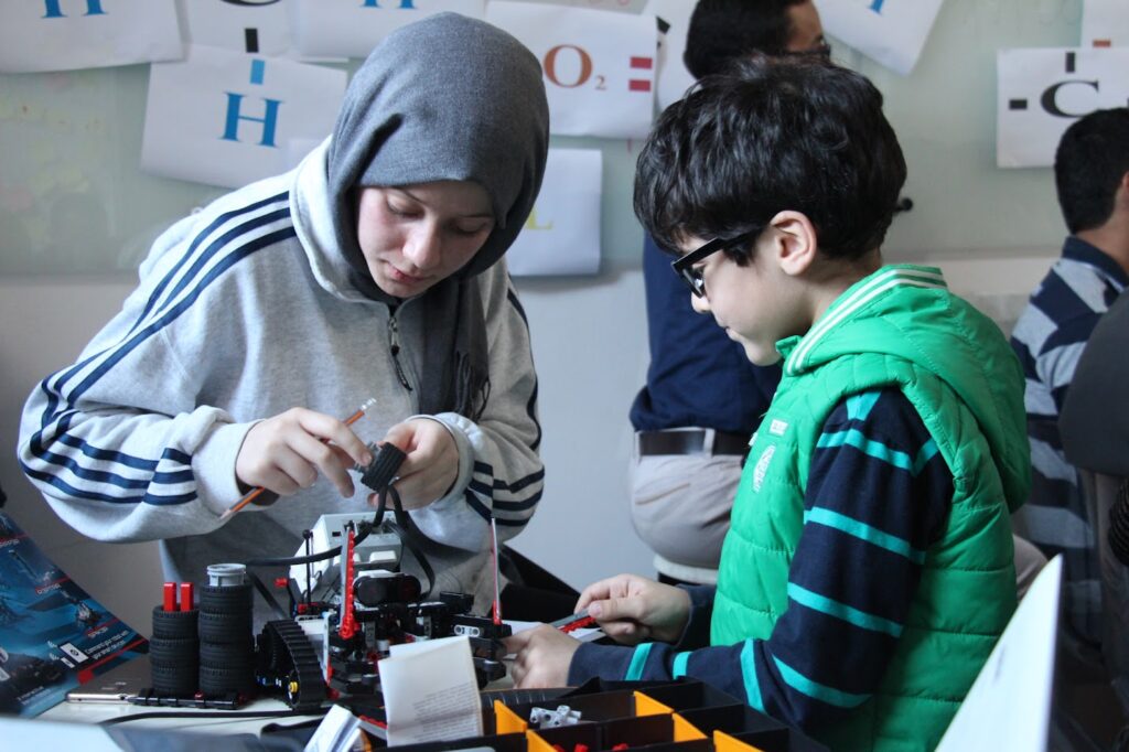 A female student and a male student working building a small robot on a table. Both are approximately elementary school age.