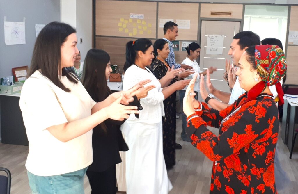 Eight adults in World Learning’s C5 + O.N.E. Ed program form two lines facing each other. Some raise their hands in high fives, and others point their fingers.