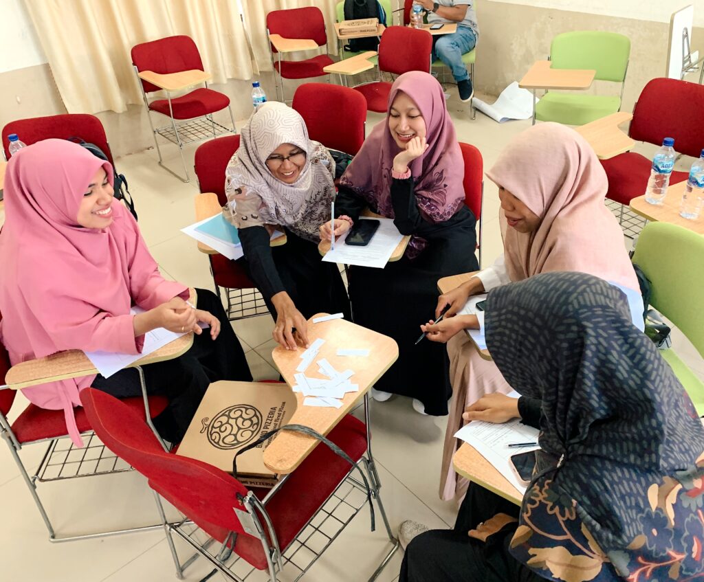 Five women sitting in desks in a circle, doing an activity with strips of paper. They are taking part in World Learning's English Learning Teacher Training program.