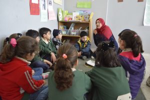 A teacher sits in a group of students reading.