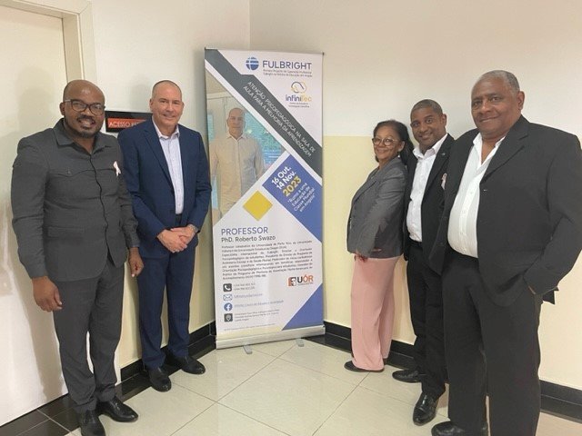 Five adults stand in front of a poster.