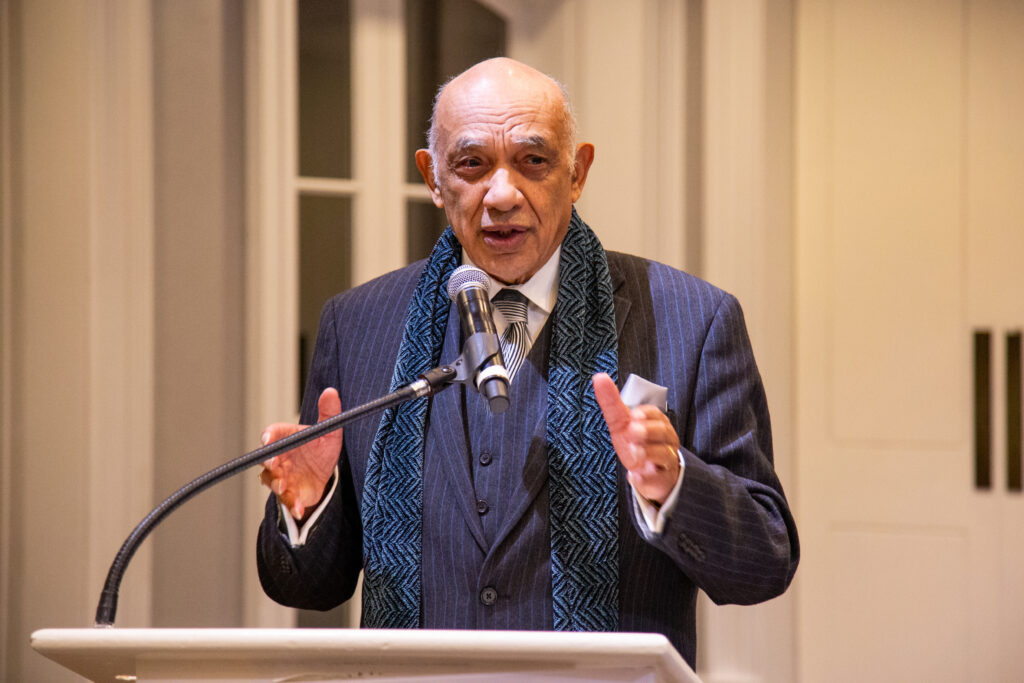 Male standing at a podium talking into a microphone. His hands are raised, gesturing.