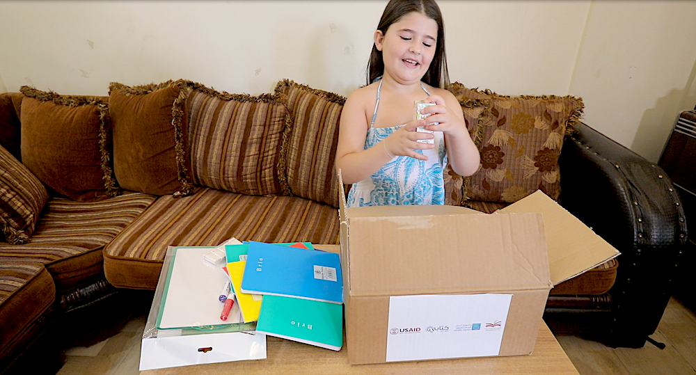 A young girl opens a box of educational supplies.